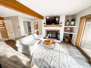 A modern living room with a white sofa, a wooden coffee table, and a fireplace.