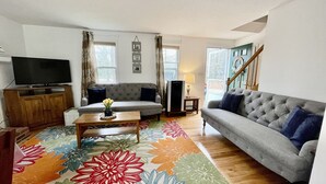 Ein Wohnzimmer mit grauem Sofa, einem Fernseher auf einer Holzkommode, einem Couchtisch mit einer Vase und einem gemusterten Teppich.