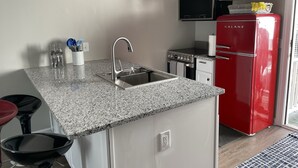 Een kleine keuken met een granieten aanrecht, een roestvrijstalen spoelbak, een rode koelkast en een magnetron boven het fornuis.