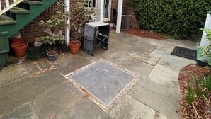 Een bakstenen gebouw met een groene trap die leidt naar een balkon, omgeven door potplanten en een stenen terras.