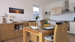 A modern kitchen with a dining area, featuring a wooden table, wicker chairs, and a view of the city. - Captains-TERRACE- Photovoltaic- Fireplace-large quiet terrace (Göhren-Lebbin)