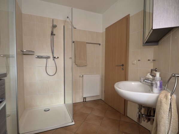 Une salle de bain moderne avec une douche à parois de verre, un lavabo blanc et une porte en bois.
