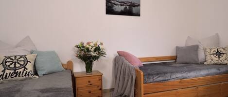 A bedroom with two beds, a nightstand with a vase of flowers, and a wall-mounted picture.