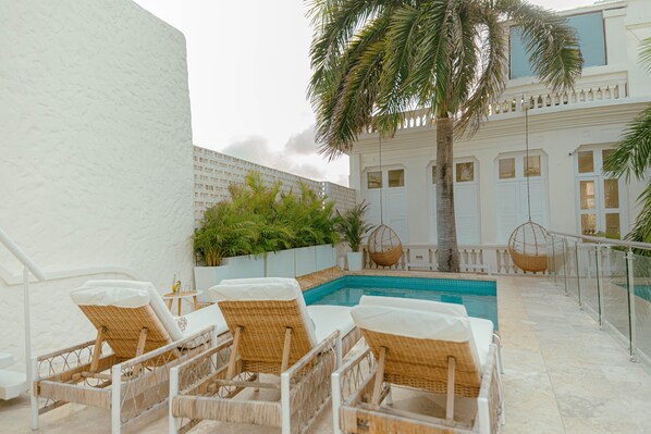 A poolside area with wicker lounge chairs, a palm tree, and a building with white walls and windows. - Casa DiLuca Cartagena Hotel Boutique (Cartagena)