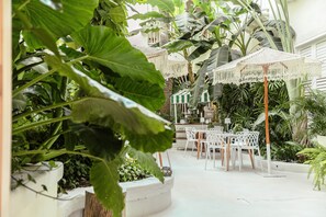 An outdoor patio area with white chairs and tables, surrounded by large green plants and a white umbrella. - Casa DiLuca Cartagena Hotel Boutique (Cartagena)