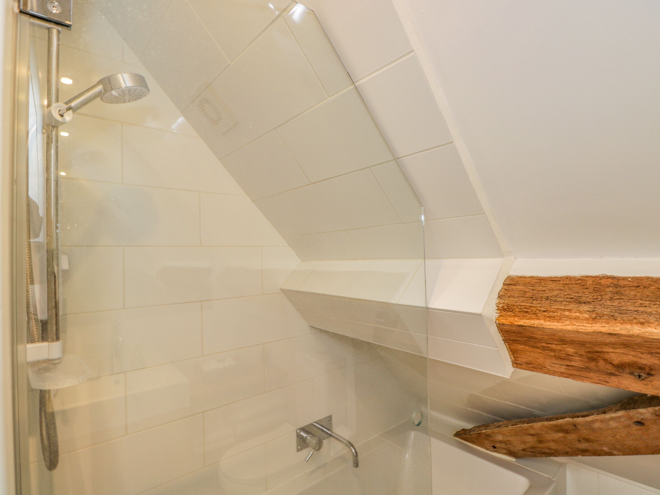 A modern bathroom with a glass shower enclosure, a bathtub, and a wooden shelf.