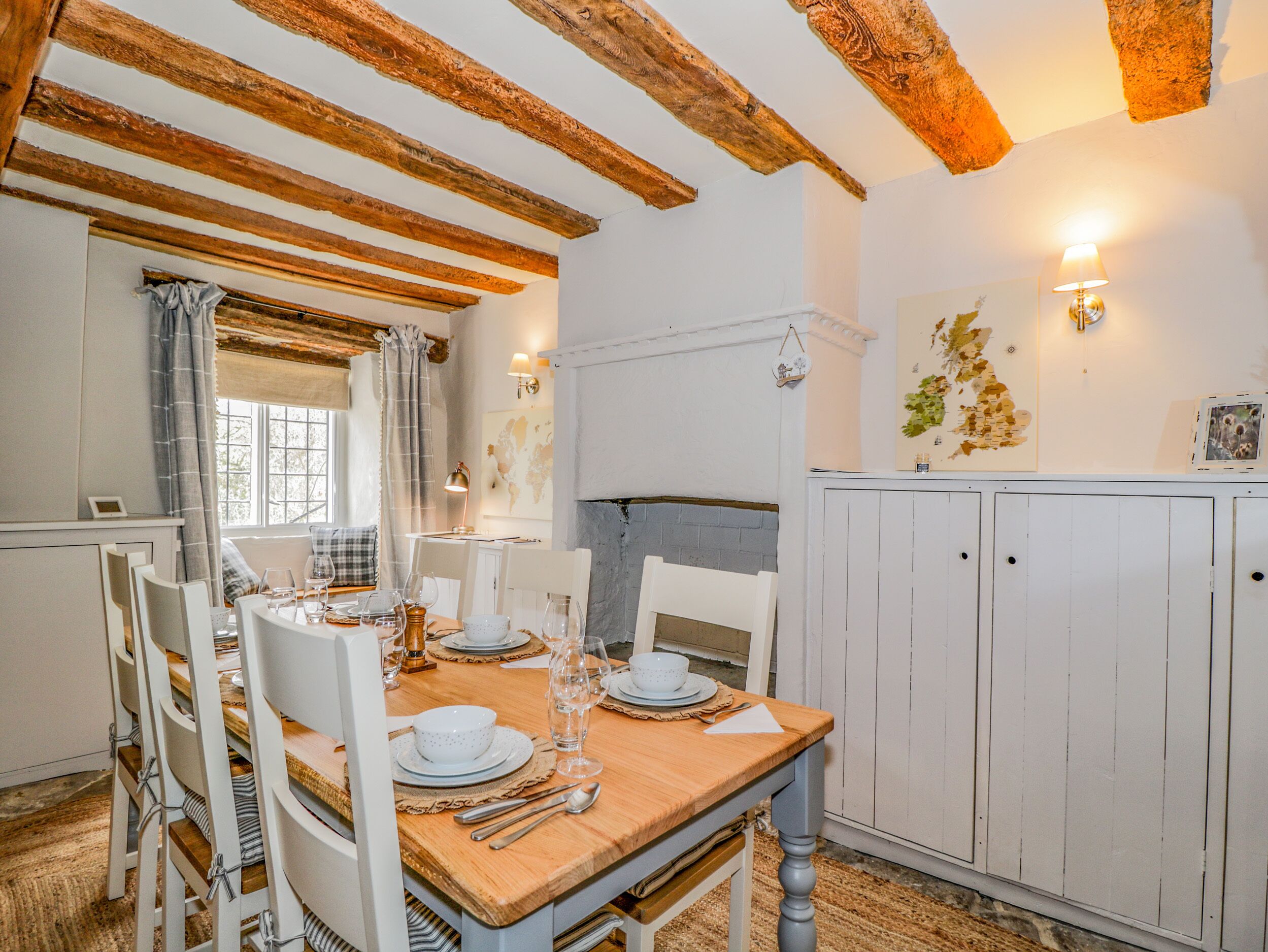 A dining area with a wooden table set for four, white chairs, and a white cabinet with doors.