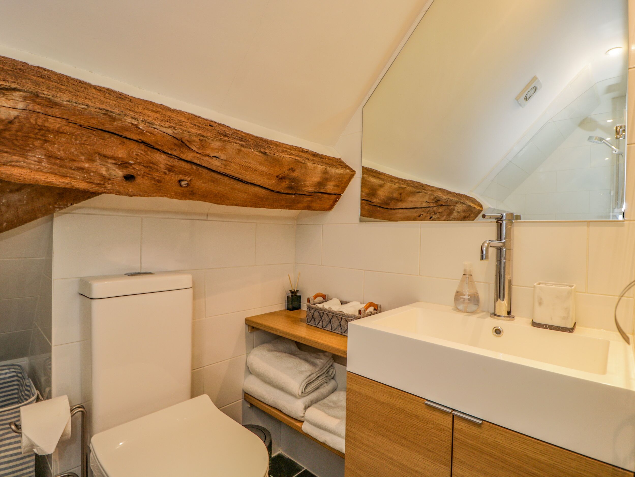 A bathroom with a wooden ceiling beam, a white toilet, a sink with a mirror, and a towel rack.