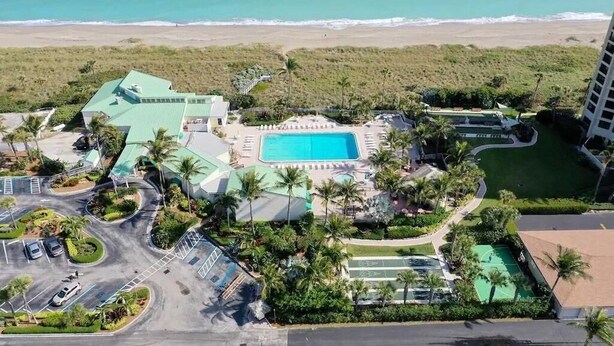 Vue aérienne d’un complexe hôtelier doté d’une piscine, d’un court de tennis et offrant une vue sur la plage.