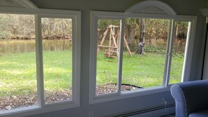 A room with large windows overlooking a grassy area with a wooden swing set. - Cabin on Jordan River! (East Jordan)