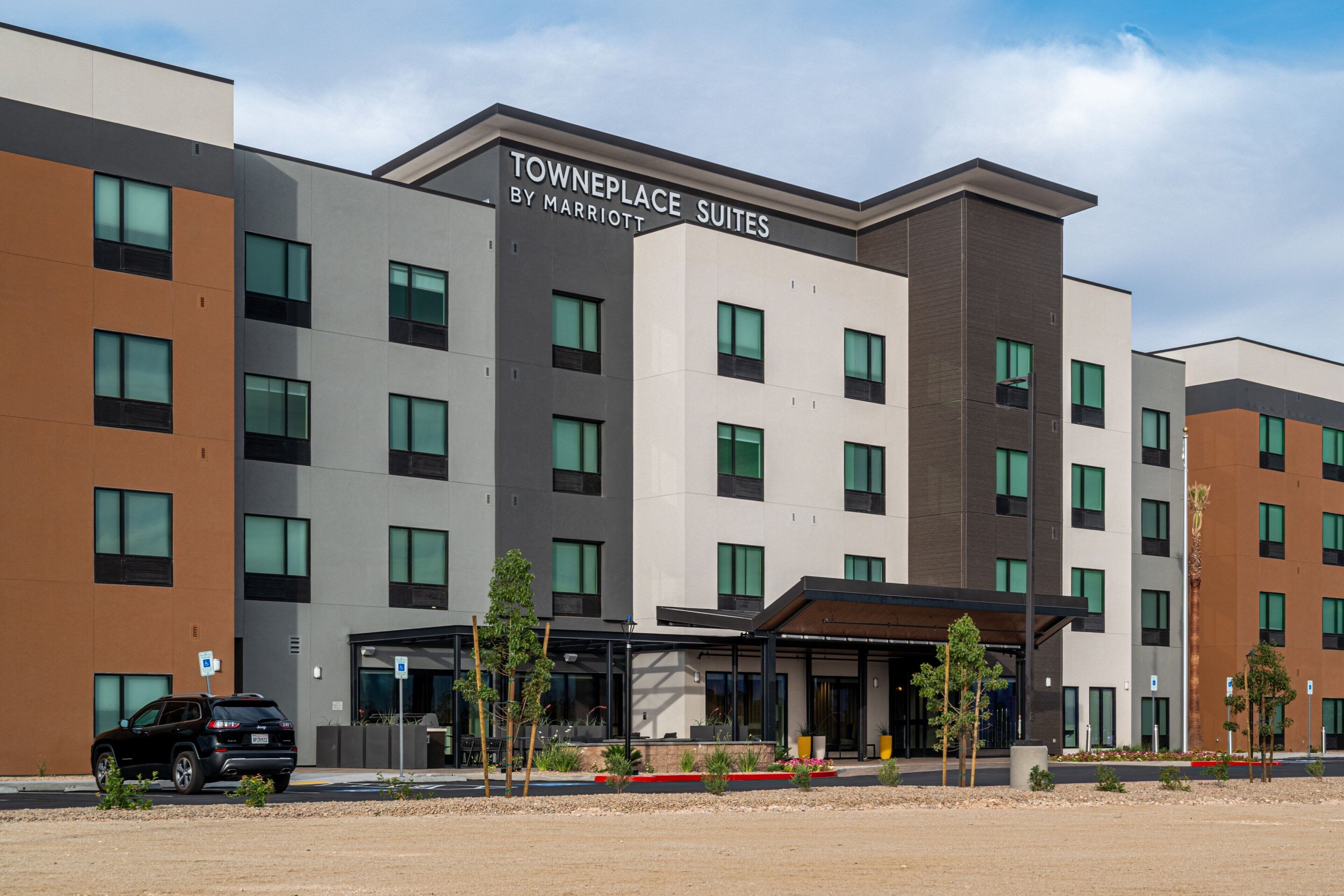 Un hôtel à plusieurs étages, avec une enseigne indiquant « Towneplace Suites by Marriott » et un parking où est stationné un SUV noir.