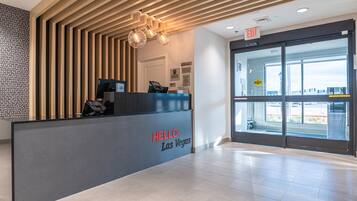 A reception desk with a "HELLO Las Vegas" sign, a modern wooden slat ceiling, and a glass door entrance.