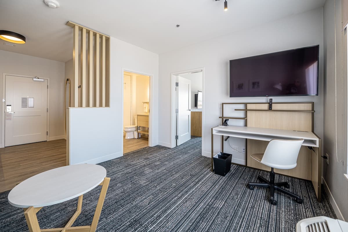 A modern hotel room with a desk, chair, and a flat-screen TV mounted on the wall.