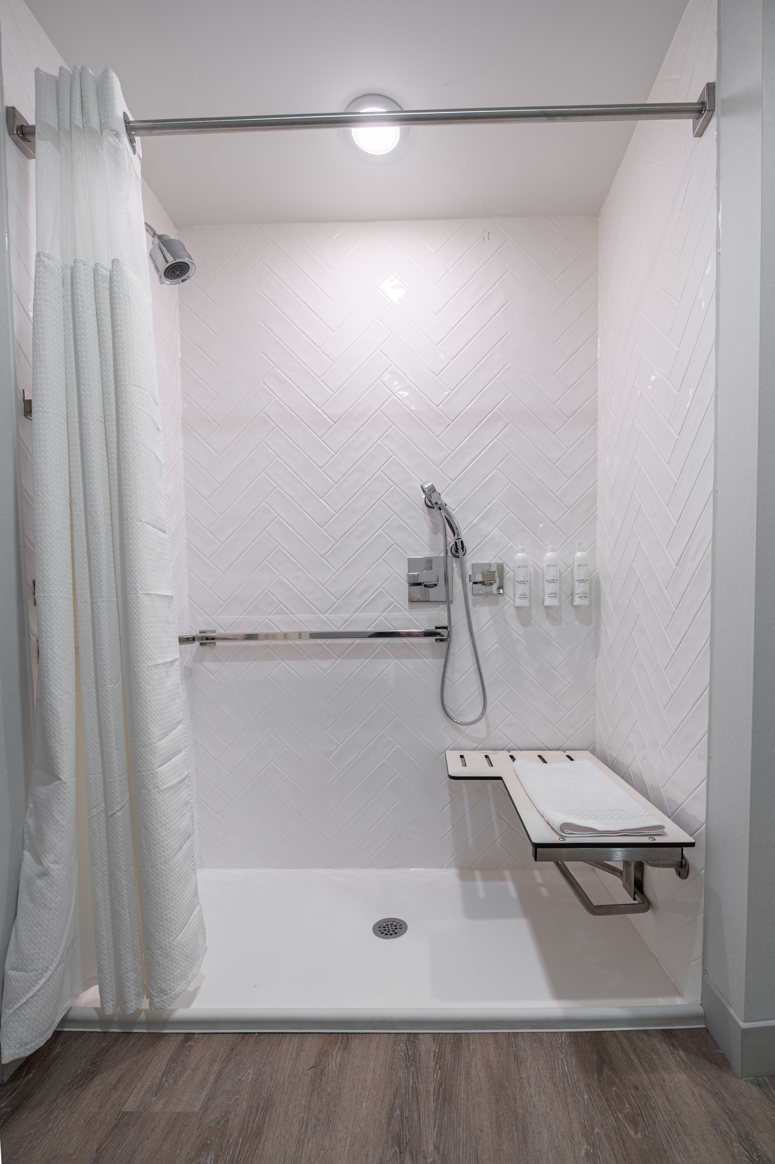 A walk-in shower with a glass door, a showerhead, a handheld shower attachment, and a small shelf with toiletries.