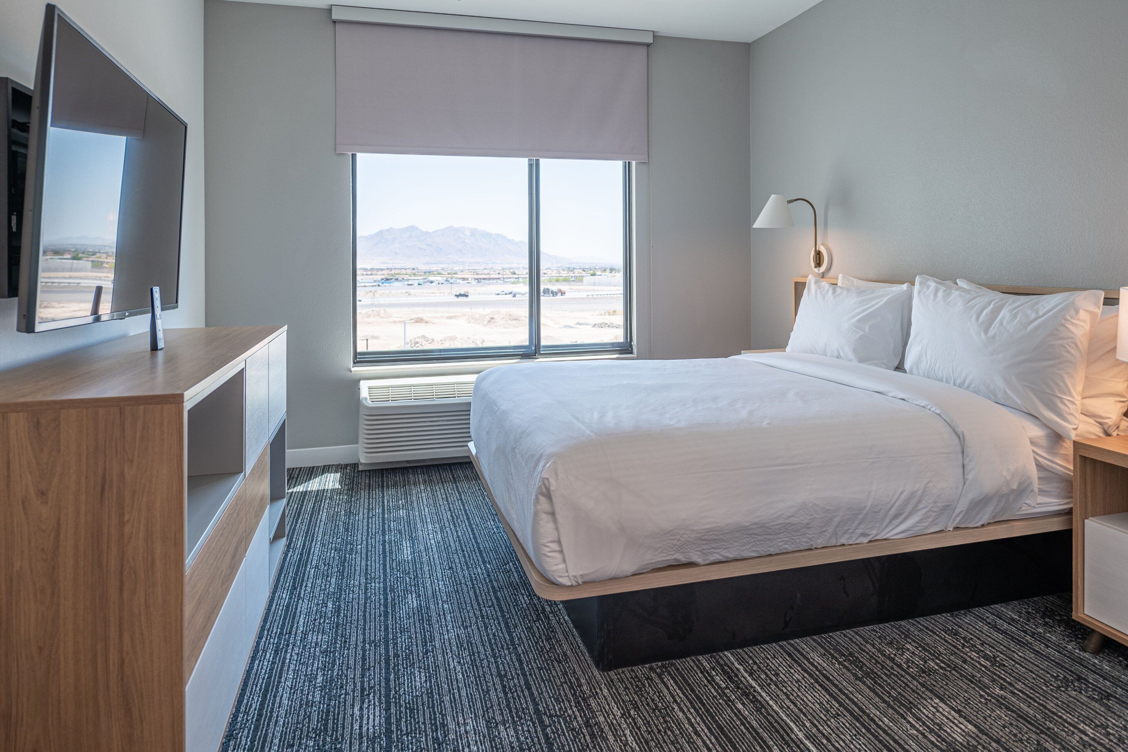A hotel room with a bed, a TV, a window with a view of mountains, and a desk with a lamp.