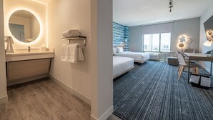 A modern hotel room with a bathroom featuring a round mirror, a sink, and a towel rack. The room includes a bed, a desk with a chair, and a large window offering a view. - TownePlace Suites by Marriott Las Vegas North I-15 (Las Vegas)