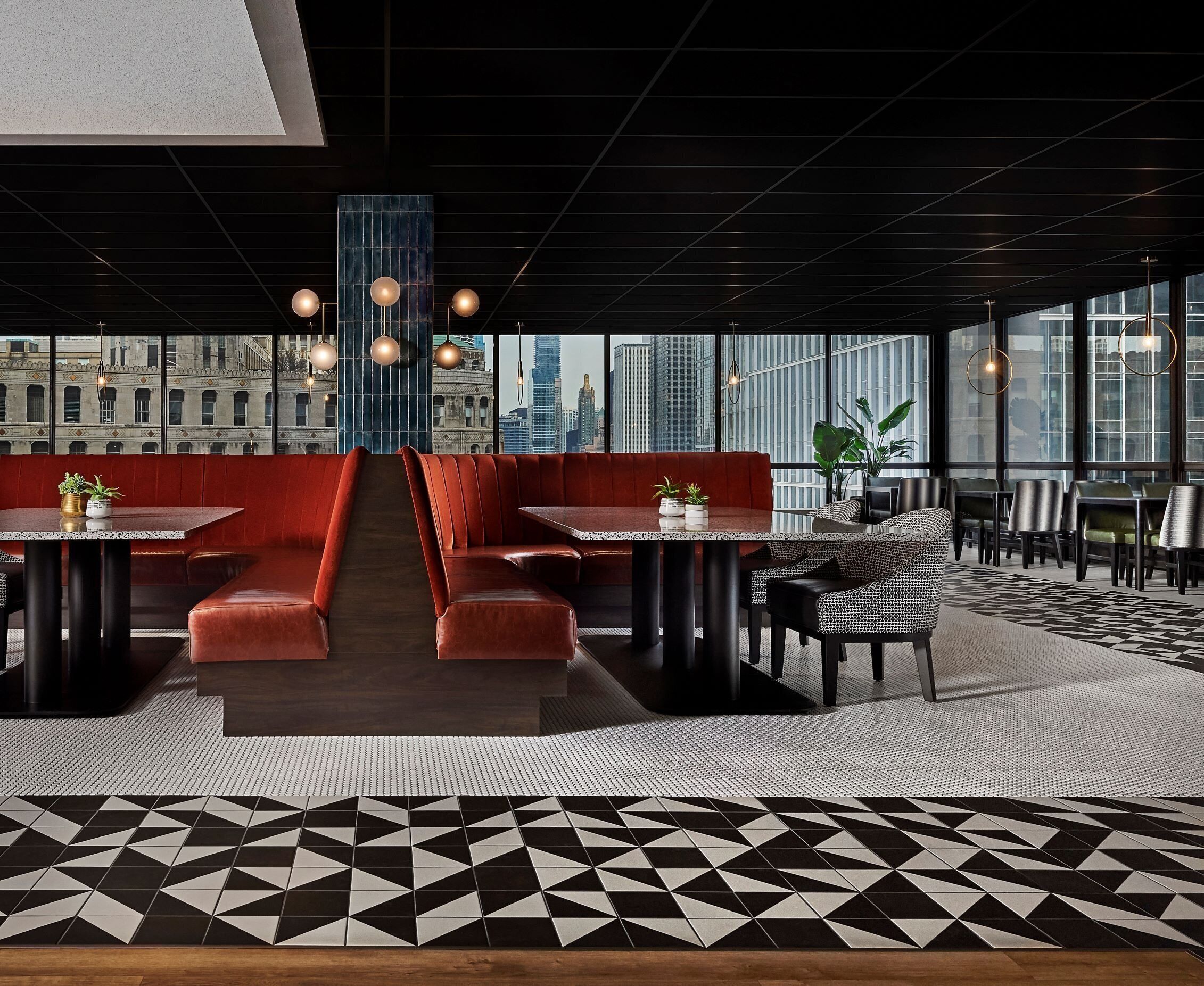 A modern restaurant with red booths, black and white patterned flooring, and city views through large windows.