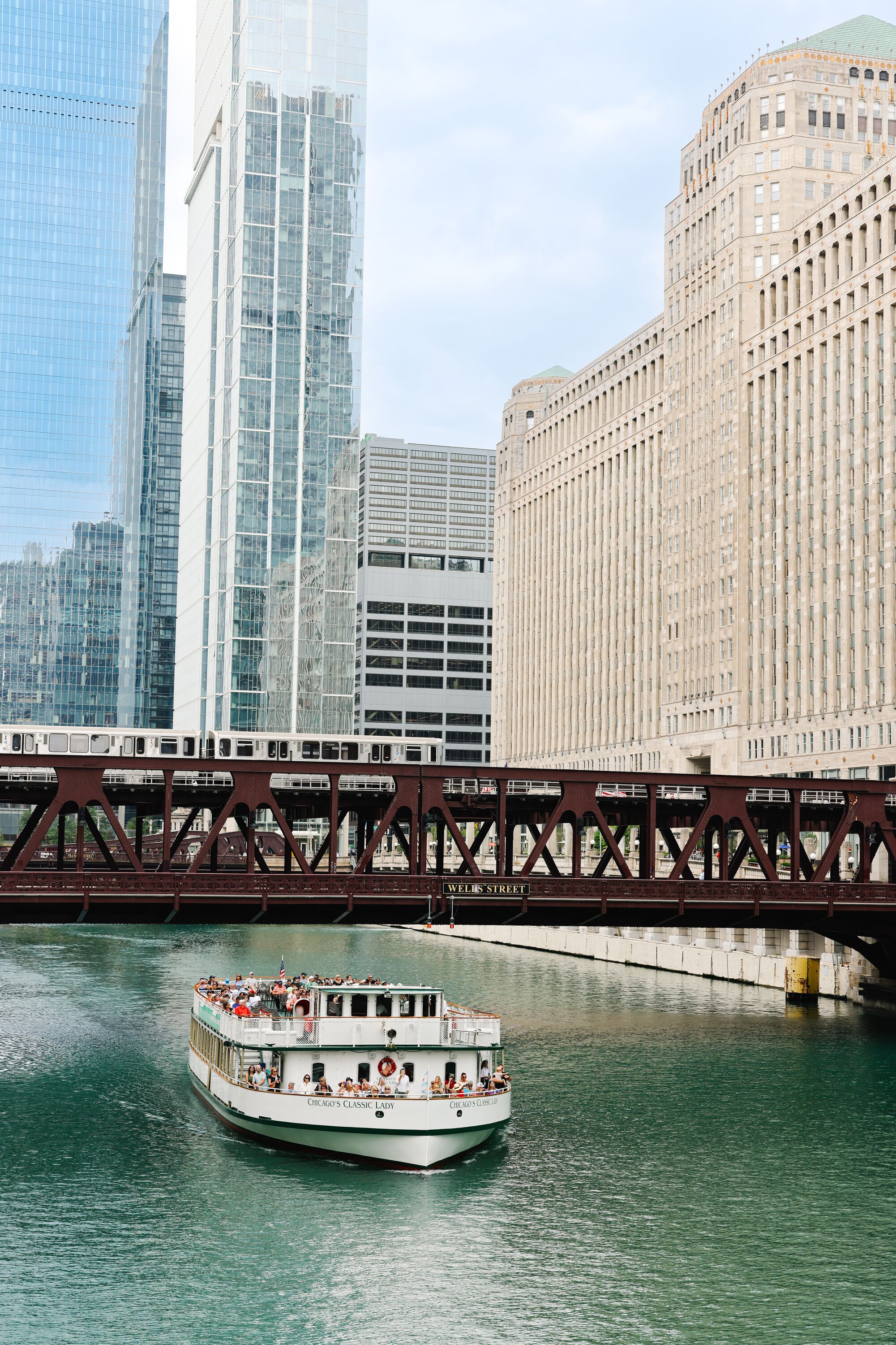 A riverboat with passengers, a bridge, and modern buildings in the background.