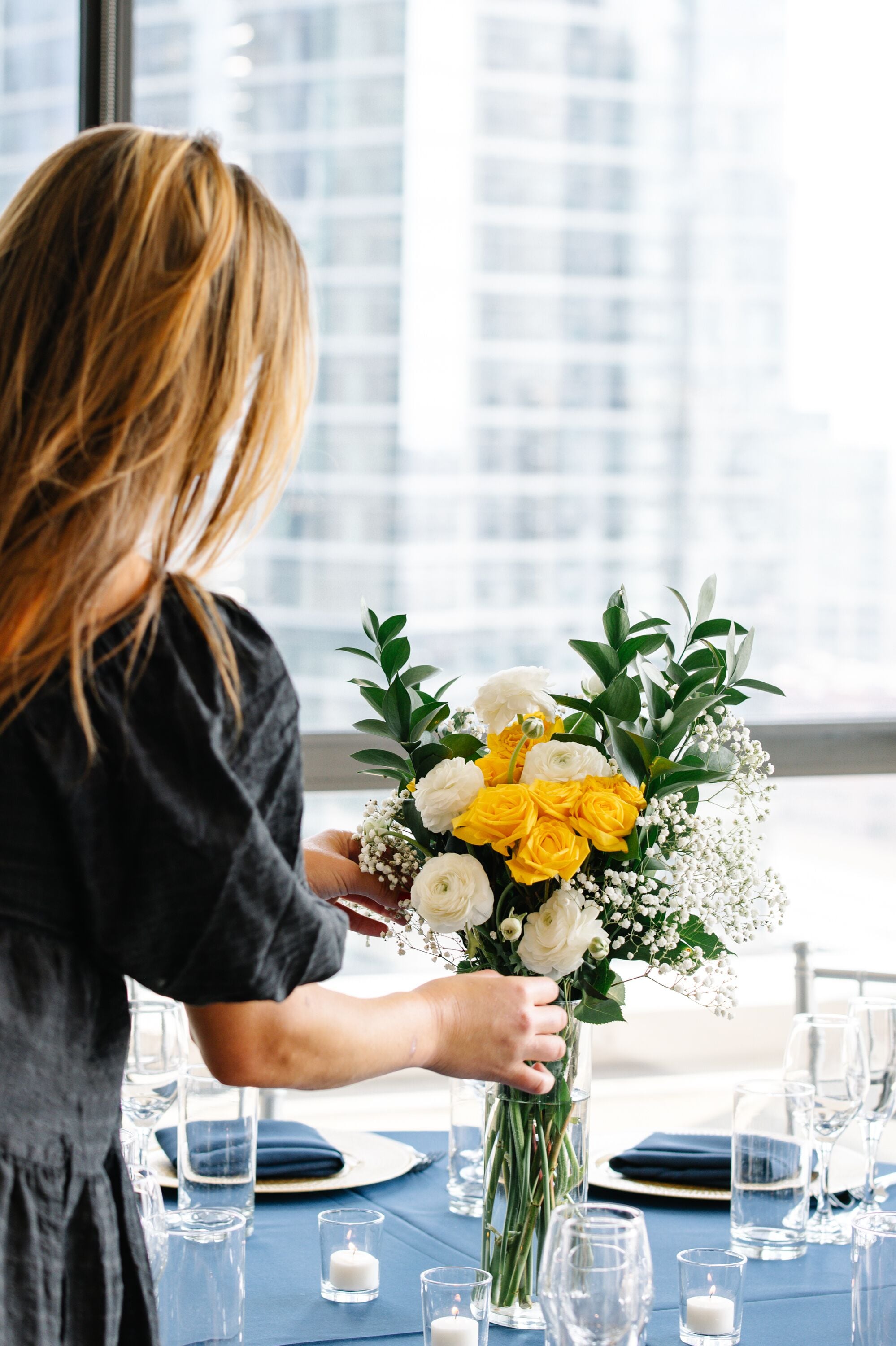En person som arrangerar en blomsterbukett på ett bord med genomskinliga glasföremål och blå dukar.