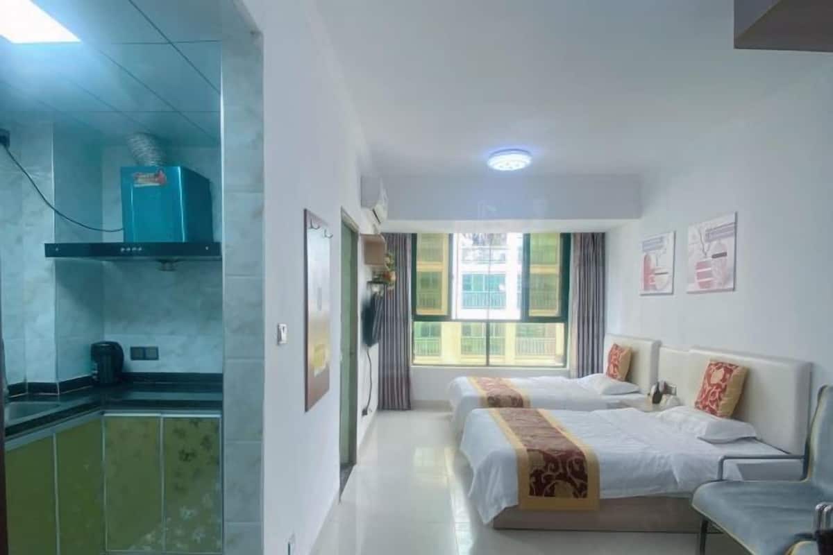 A hotel room with two beds, a kitchenette, and a window with curtains.
