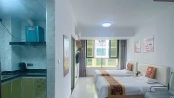 Quarto de hotel com duas camas, uma cozinha compacta e uma janela com cortinas.