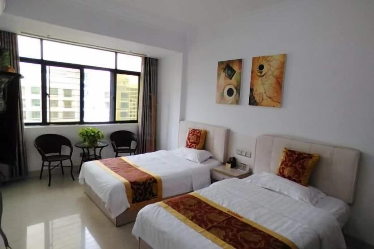A hotel room with two beds, a small table, chairs, and artwork on the wall.