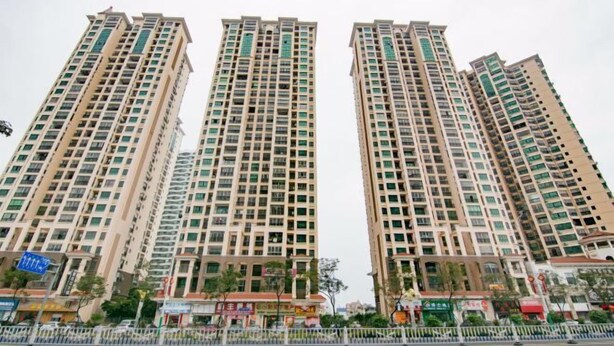 Tres edificis residencials alts, amb nombrosos pisos i balcons, envoltats de comerços i una zona tancada per una tanca.