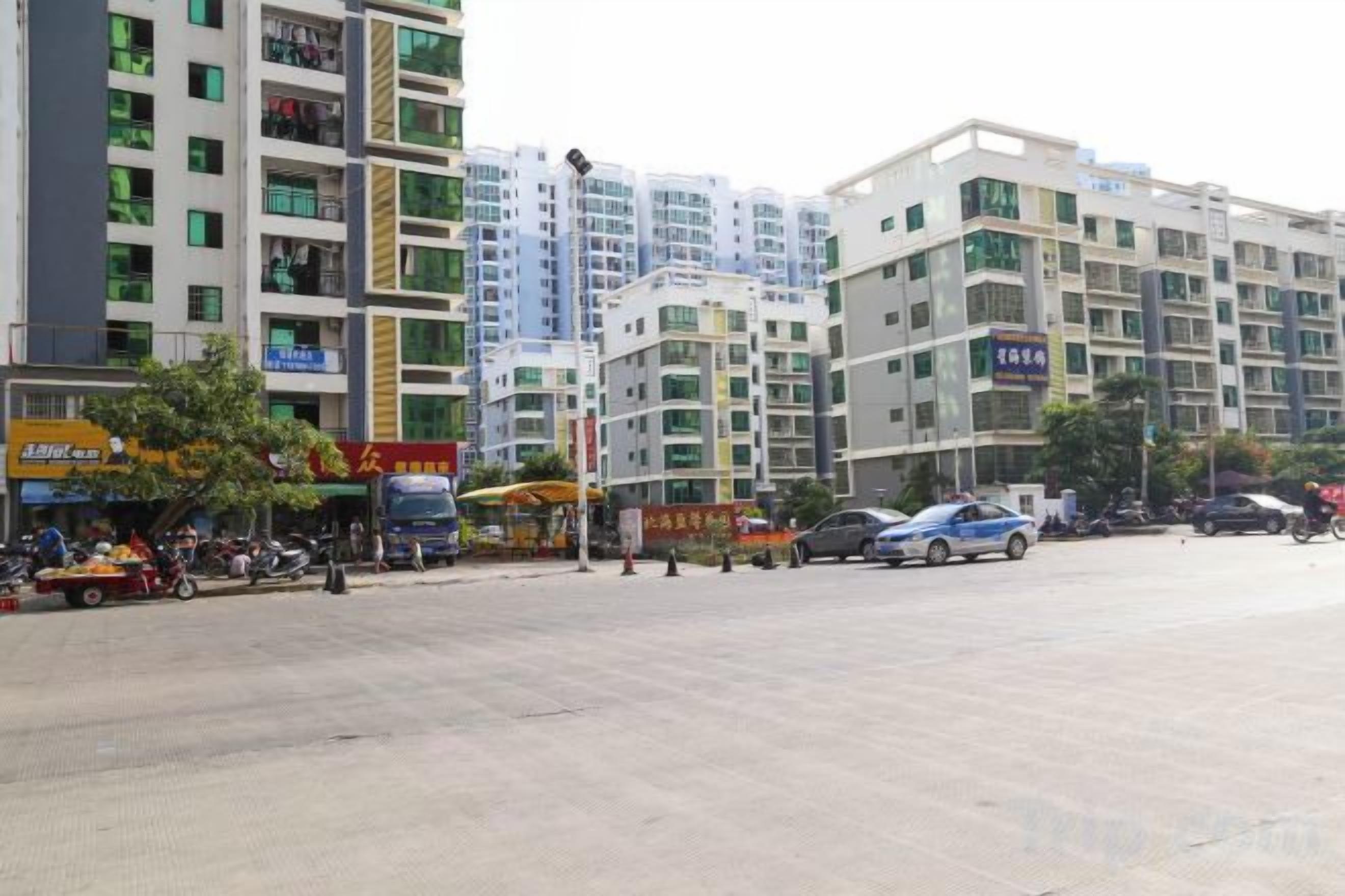 Un edificio de varios pisos con comercios en la planta baja, un área de estacionamiento y cielo despejado.