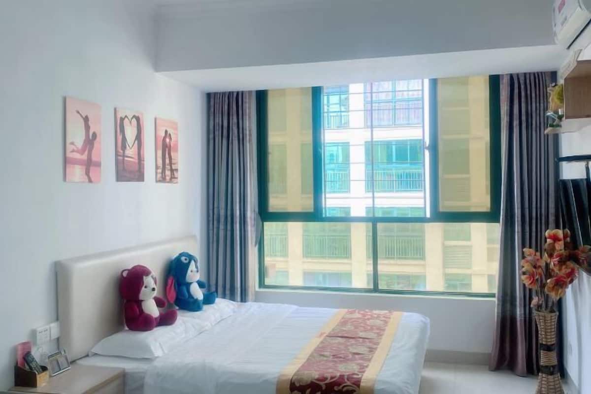 A hotel room with a bed, a nightstand, a window with curtains, and wall art.