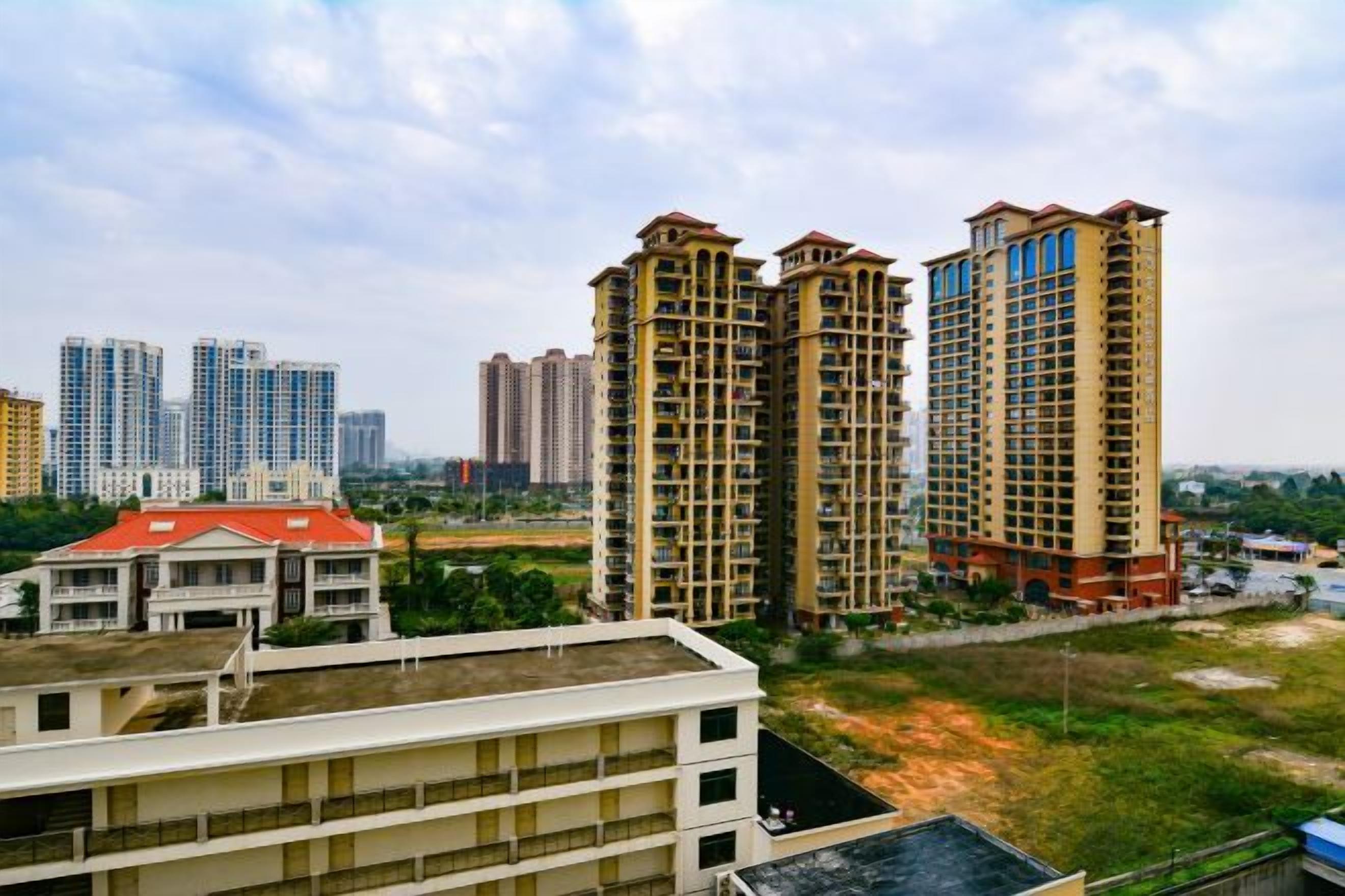 A view of high-rise residential buildings with multiple floors and balconies, surrounded by greenery and a clear sky.