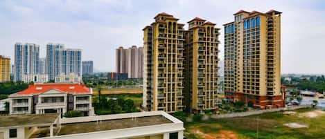 A view of high-rise residential buildings with multiple floors and balconies, surrounded by greenery and a clear sky.