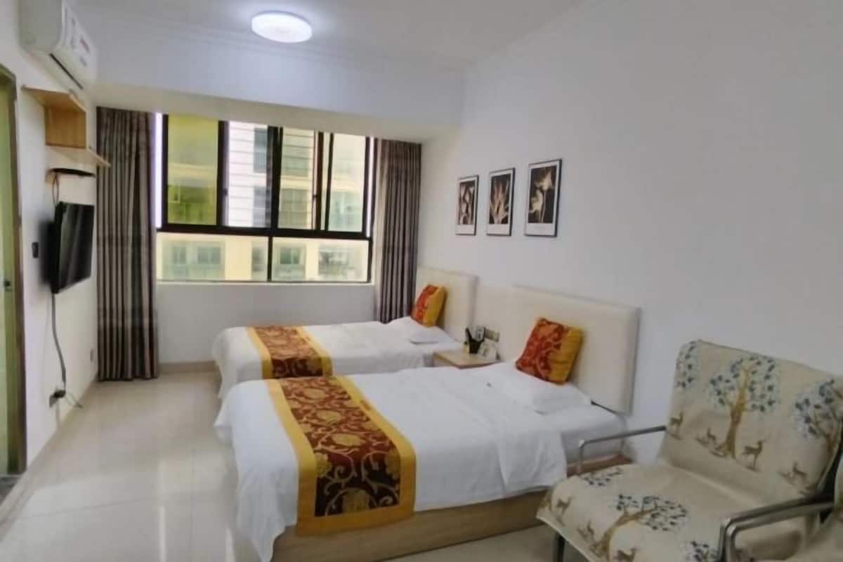 A hotel room with two beds, a chair, a TV, and a window with curtains.