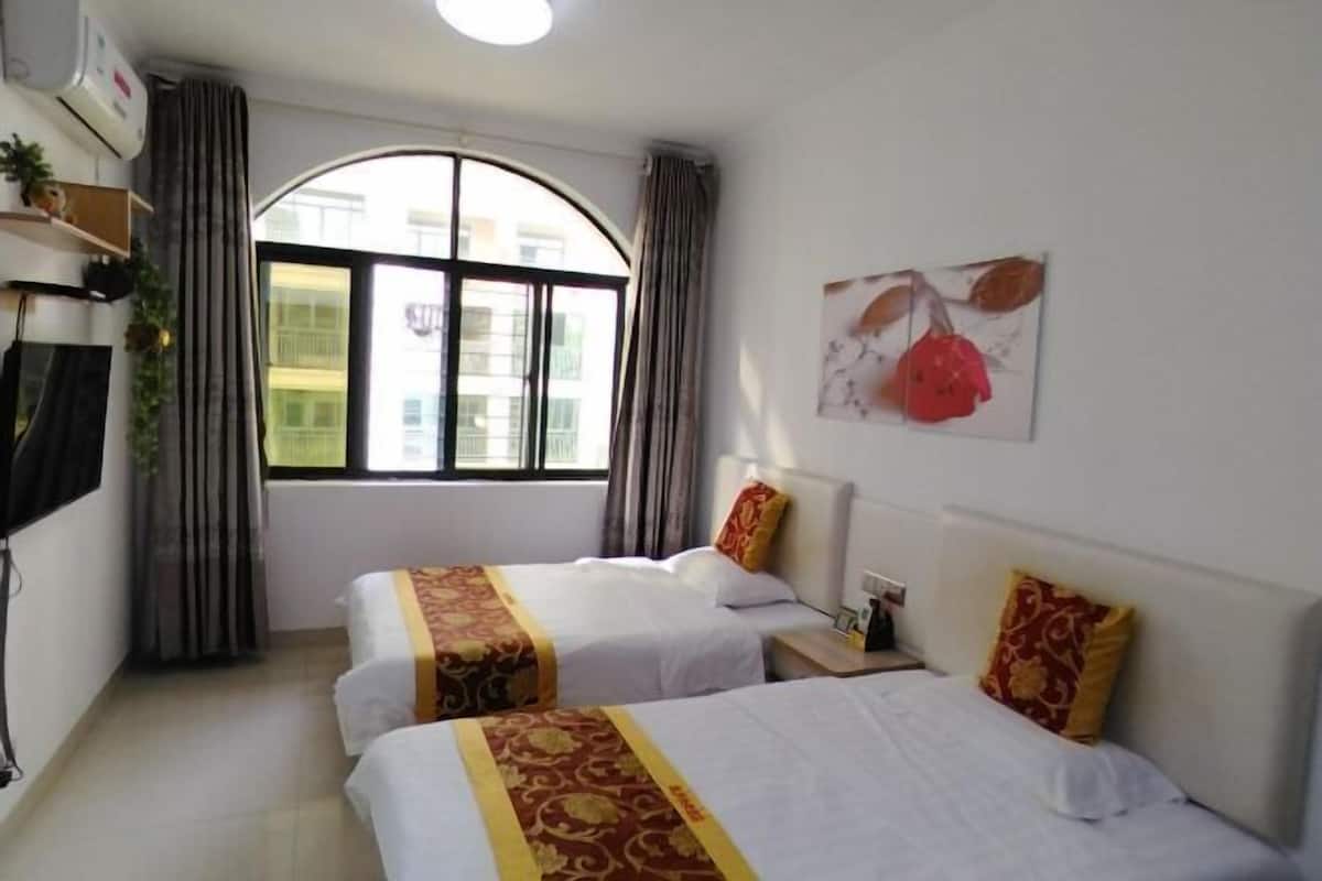 A hotel room with two beds, a large window, a wall-mounted air conditioner, and a picture of flowers.