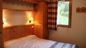 A wooden room with a bed, two wall-mounted lamps, and a window with a plaid curtain. - 150m from ski slopes, 2nd floor, view swimming pool, fitness, swimming pool, balcony, tv, ski locker (Lanslebourg-Mont-Cenis)