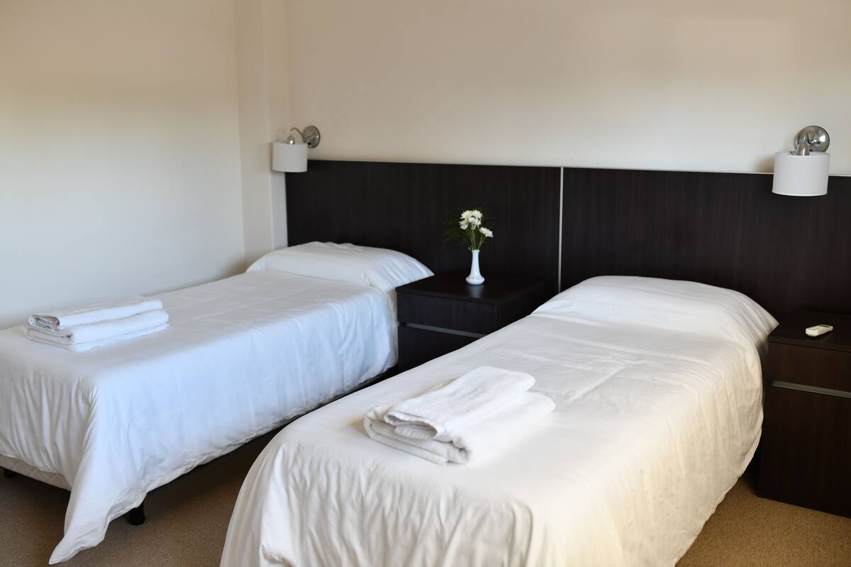 A hotel room with two single beds, a nightstand with a lamp, and a vase with flowers.