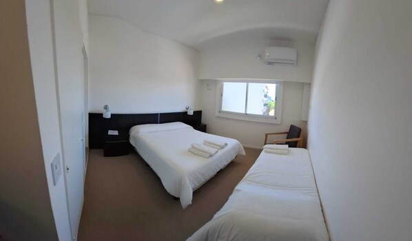 A bedroom with two beds, a window, and an air conditioning unit.