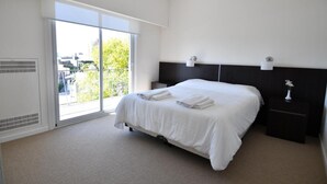 Habitación de hotel con una cama grande, una mesita de noche, una lámpara de pared y un ventanal corredero que da a un balcón.