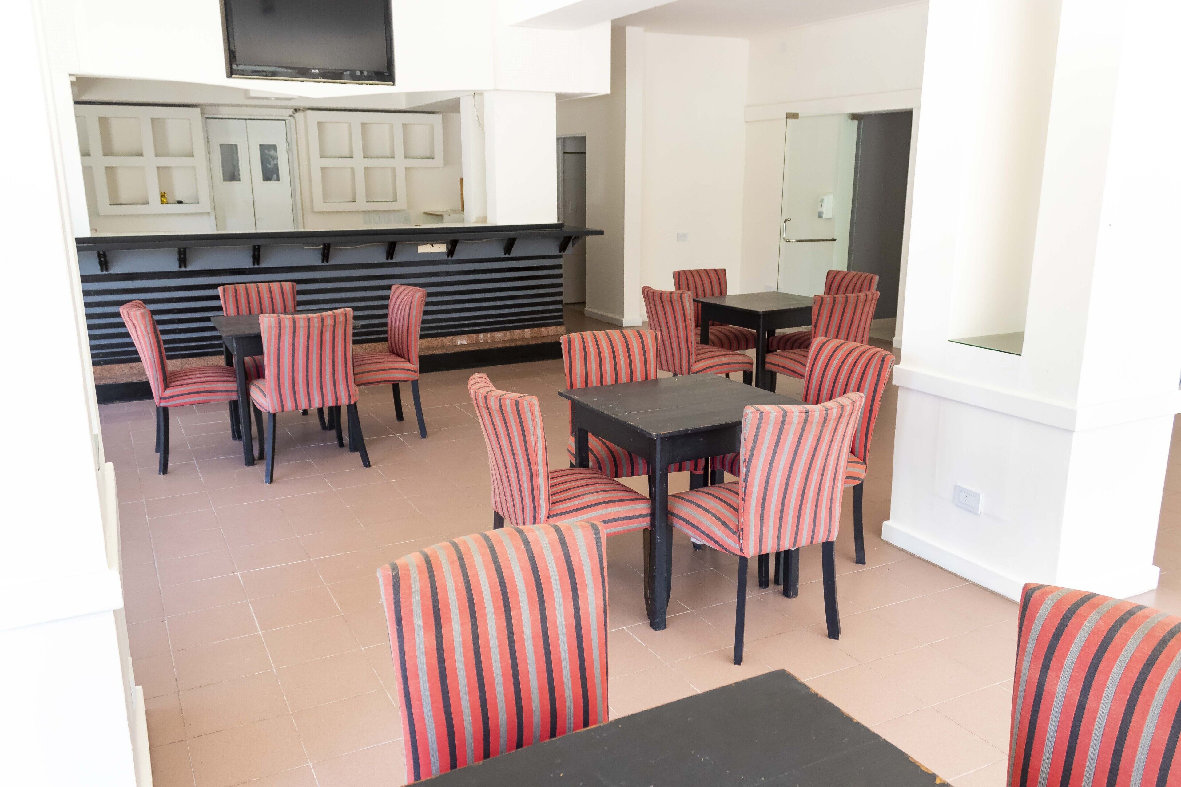 A dining area with striped chairs and tables, a kitchen with cabinets, and a flat-screen TV mounted above the counter.