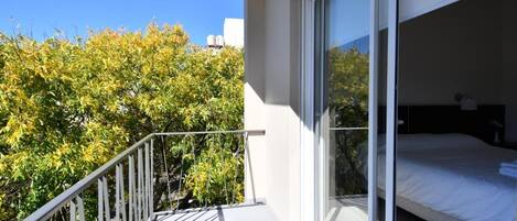 A balcony with a metal railing, a bed with white bedding, and a sliding glass door leading to a bedroom.
