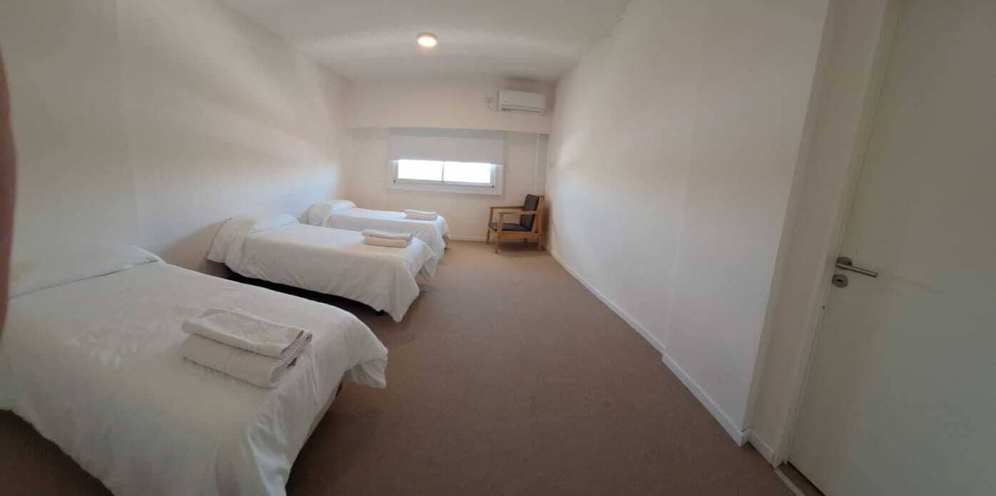 A room with three single beds, a wooden chair, and a window.