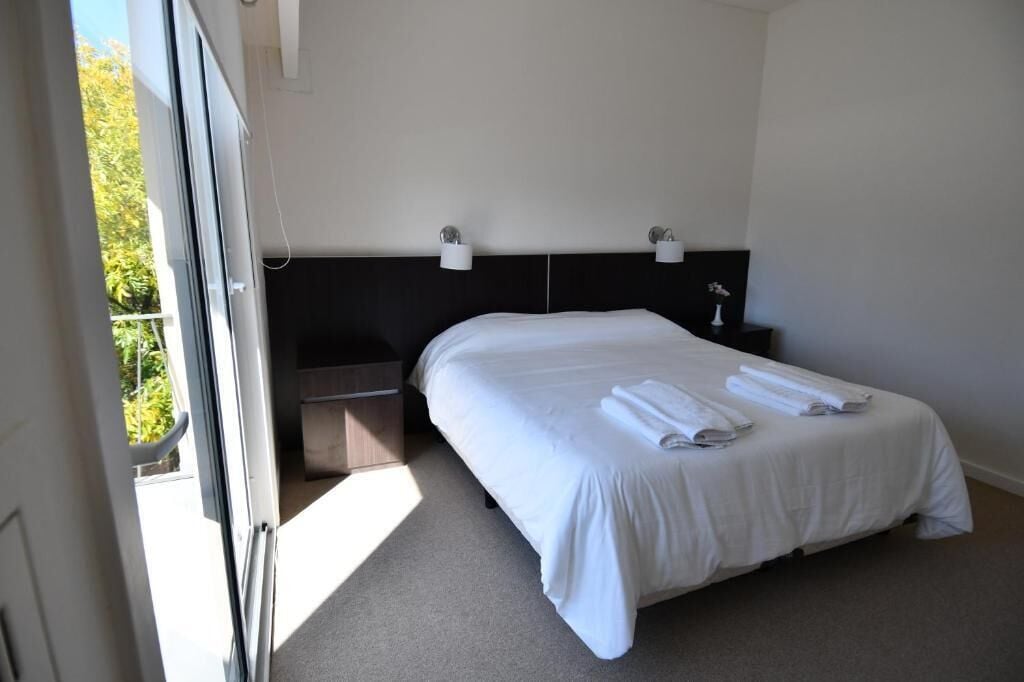 A hotel room with a bed, bedside tables, and a view through an open door.