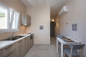 A compact kitchen with a window, a dining area with a table and chairs, and a hallway leading to another room.