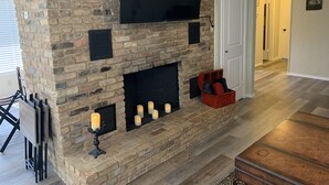 A living room with a brick fireplace, a flat-screen TV mounted above it, and a wooden coffee table. - Clair de Lune, Lake Front on Lake Palestine  (Chandler)