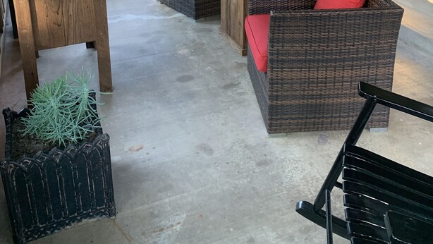 A covered patio area with wicker furniture, red cushions, and a concrete floor. - Clair de Lune, Lake Front on Lake Palestine  (Chandler)