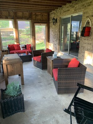 Un patio couvert aménagé avec des meubles en osier, des coussins rouges et un sol en béton.
