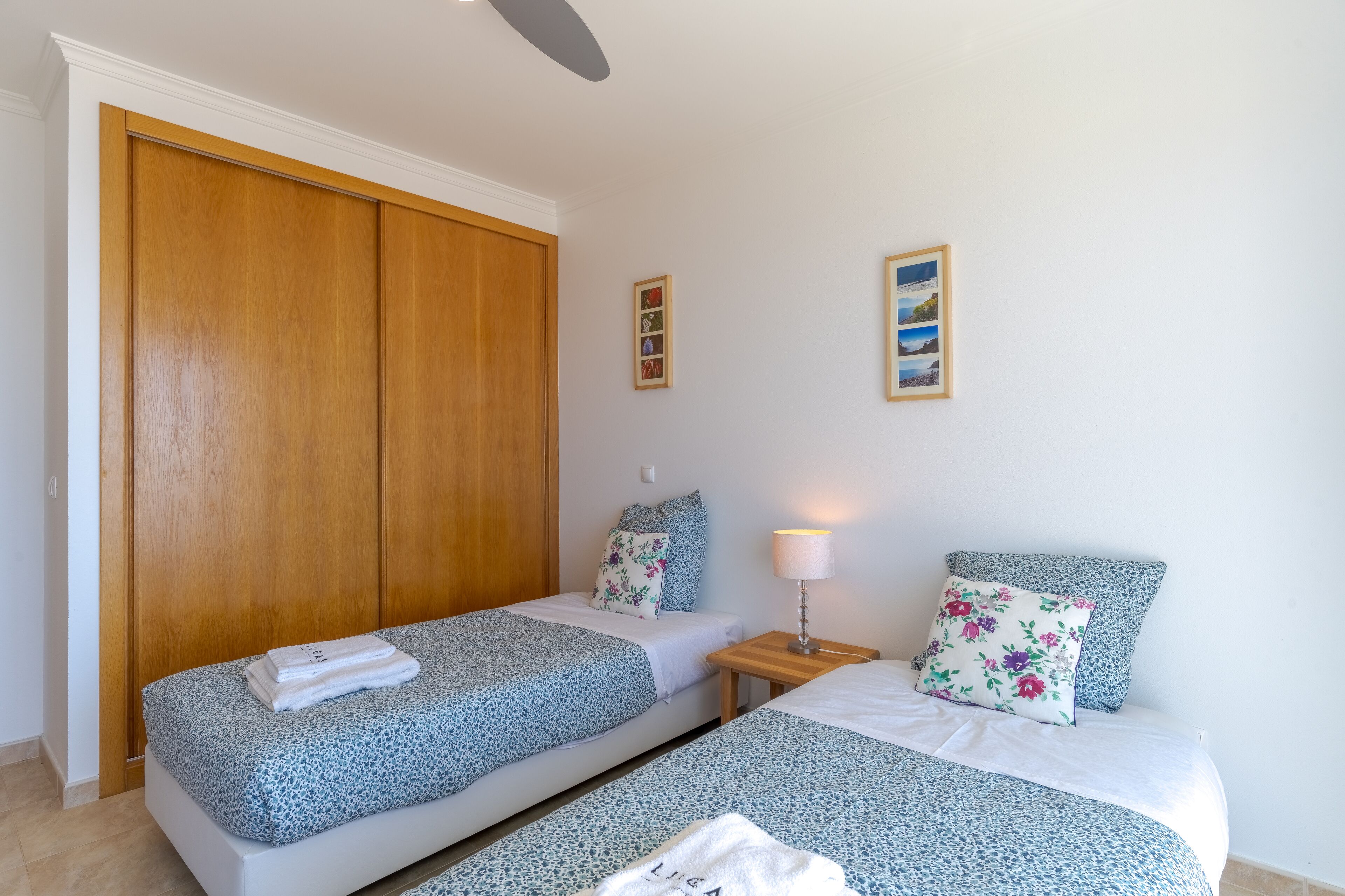 A bedroom with two beds, wooden wardrobe, and framed pictures on the wall.