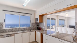 Una cocina moderna con encimeras de granito, armarios blancos y un amplio ventanal con vistas al mar.