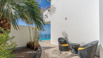 Un patio con un muro blanco, una pequeña piscina y dos sillas de mimbre con cojines.