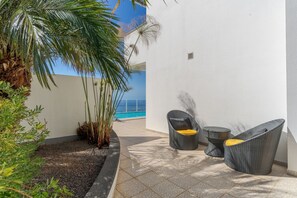 Eine Terrasse mit einer weißen Wand, einem kleinen Pool und zwei Korbstühlen mit Kissen.