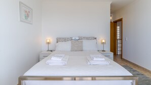 Una cama bien hecha con sábanas y toallas blancas, una mesita de noche con lámpara y un cuadro en la pared.